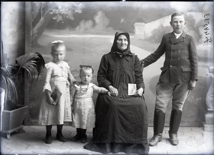Nagymama (?) unokáival. Az asszony és az egyik kislány kezében a fronton lévő fiú/édesapa fotója, Endrőd, üvegnegatív, 13x18 cm, Szabó Imre felvétele, 1910-es évek második fele, Néprajzi Múzeum, F 44533