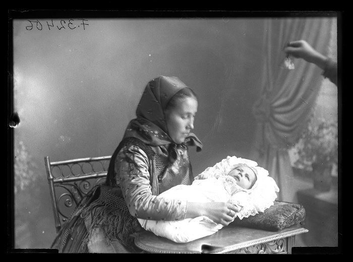 Fiatalasszony pólyással, a kép előterében egy csengő látszik, mellyel a csecsemő figyelmét irányítják, Rákospalota, üvegnegatív, 12x16,5 cm, Borsy Béla felvétele, 1914-1919 között, Néprajzi Múzeum, F 32406